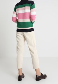 Pull en tricot à rayures horizontales vertes, roses et blanches, associé à un pantalon en velours côtelé crème et des chaussures montantes foncées à lacets.
