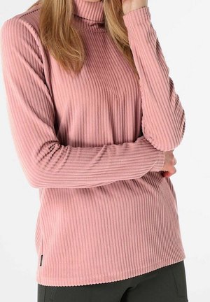 Personne portant un pull à col roulé côtelé rose à manches longues, bras croisés devant, sur un fond clair uni.