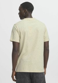 Kortermet, lysegul t-skjorte med prikkete mønster. Stoffet ser mykt ut, med en avslappet passform og enkel rund hals.