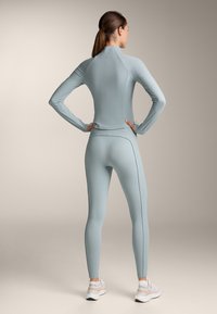 Svijetloplava dugosleeve sportska majica i odgovarajuće tajice. Glatka tekstura s kontrastnim tamnim šavovima, prilagođen dizajn. Pogodno za aktivnu odjeću.