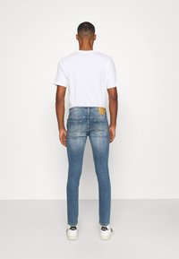 Calças jeans skinny azul com um lavagem clara, apresentando um rótulo na parte de trás e dois bolsos traseiros, combinadas com uma t-shirt branca e sapatilhas.