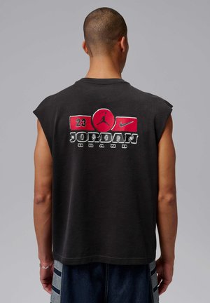 Uomo di spalle che indossa una maglietta nera senza maniche con il logo Jordan Brand rosso e bianco, il numero 23 e il logo Nike sulla schiena.