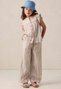 Striped outfit with a sleeveless top featuring ruffles, button closure, and wide-leg pants. Accessories include a blue bucket hat with colorful hearts.