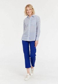 Chemise blanche à boutons avec un motif floral bleu, associée à un pantalon bleu éclatant et des sneakers blanches. Tissu lisse, coupe décontractée.