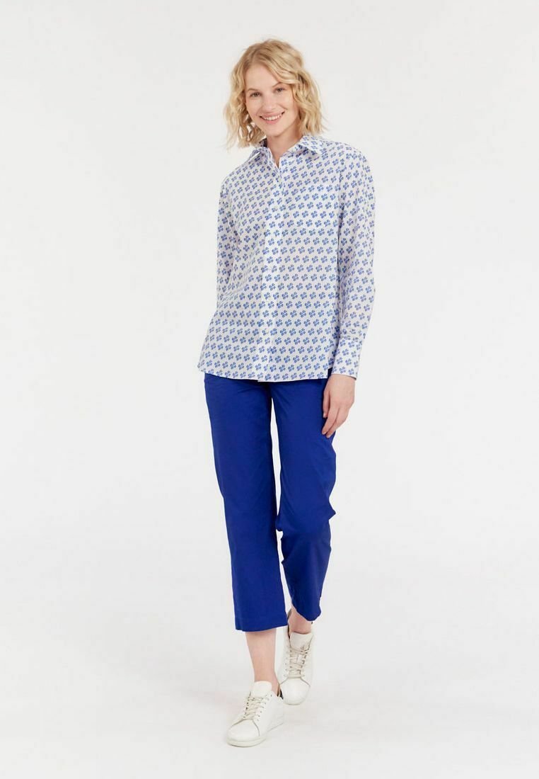 Chemise blanche à boutons avec un motif floral bleu, associée à un pantalon bleu éclatant et des sneakers blanches. Tissu lisse, coupe décontractée.