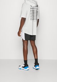 Lichtgrijze hoodie met een zwarte "BUSINESS HOURS" graphic op de achterkant, gecombineerd met zwart-witte shorts en meerkleurige sneakers.