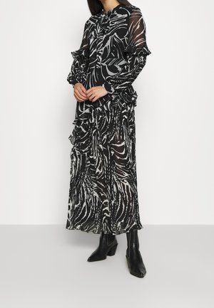 Sort-hvid gennemsigtig maxikjole med zebra-stribet mønster, flæseærmer og en bindebåndsdetalje ved halsen, kombineret med spidse sorte støvler.