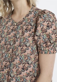 Floral blouse featuring a colorful pattern with puffed short sleeves, a V-neck, and small buttons, made from soft fabric.