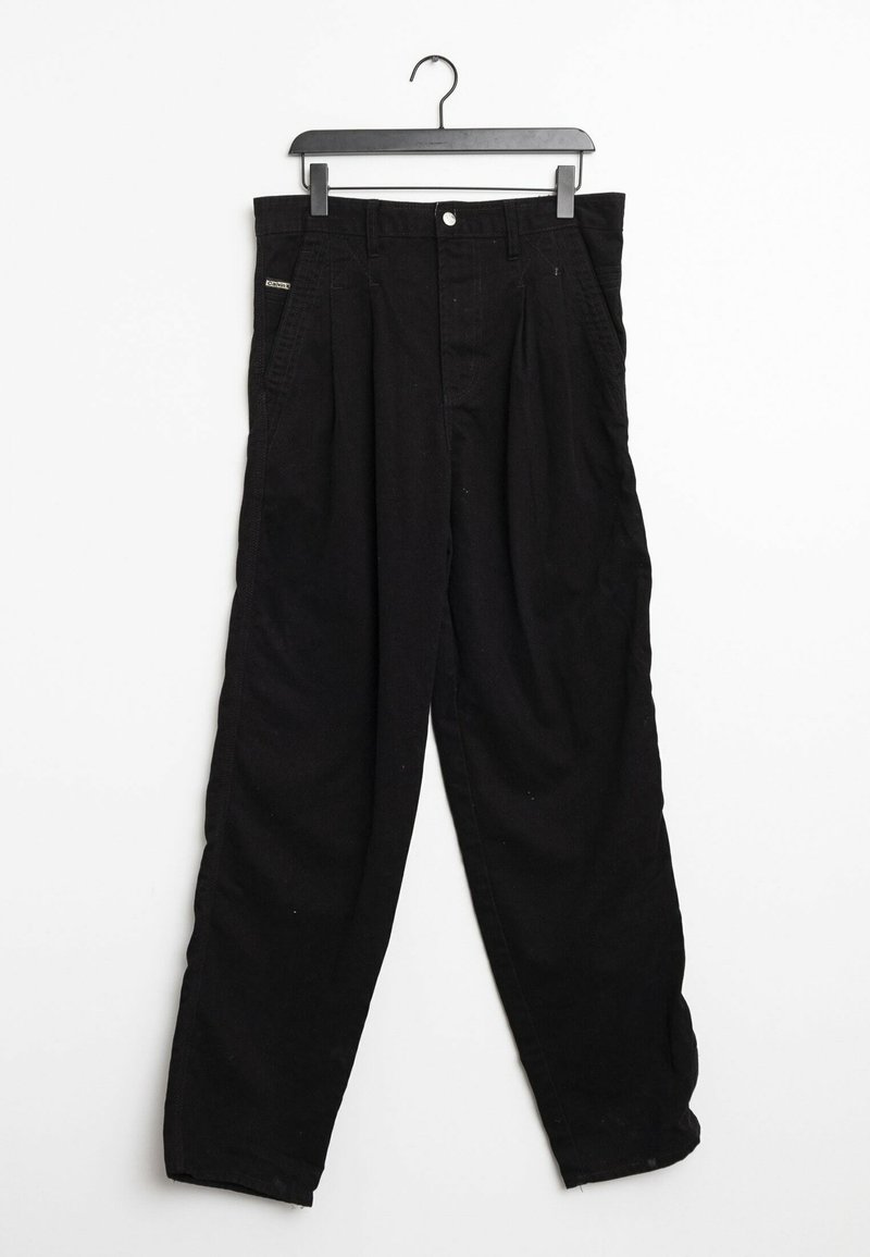 Pantalones de algodón negros con un corte holgado, que presentan pinzas frontales, un cierre de botón y bolsillos a los lados. Colgados en una percha negra.