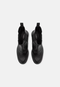 Bottes en cuir noir pour homme avec des détails perforés, des panneaux latéraux élastiques et une languette à l'arrière pour un enfilage facile. Semelle en caoutchouc plate.