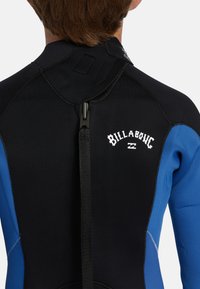 Mutino nero e blu con una texture liscia, chiusura a zip e il logo "Billabong" in bianco sulla parte superiore della schiena.