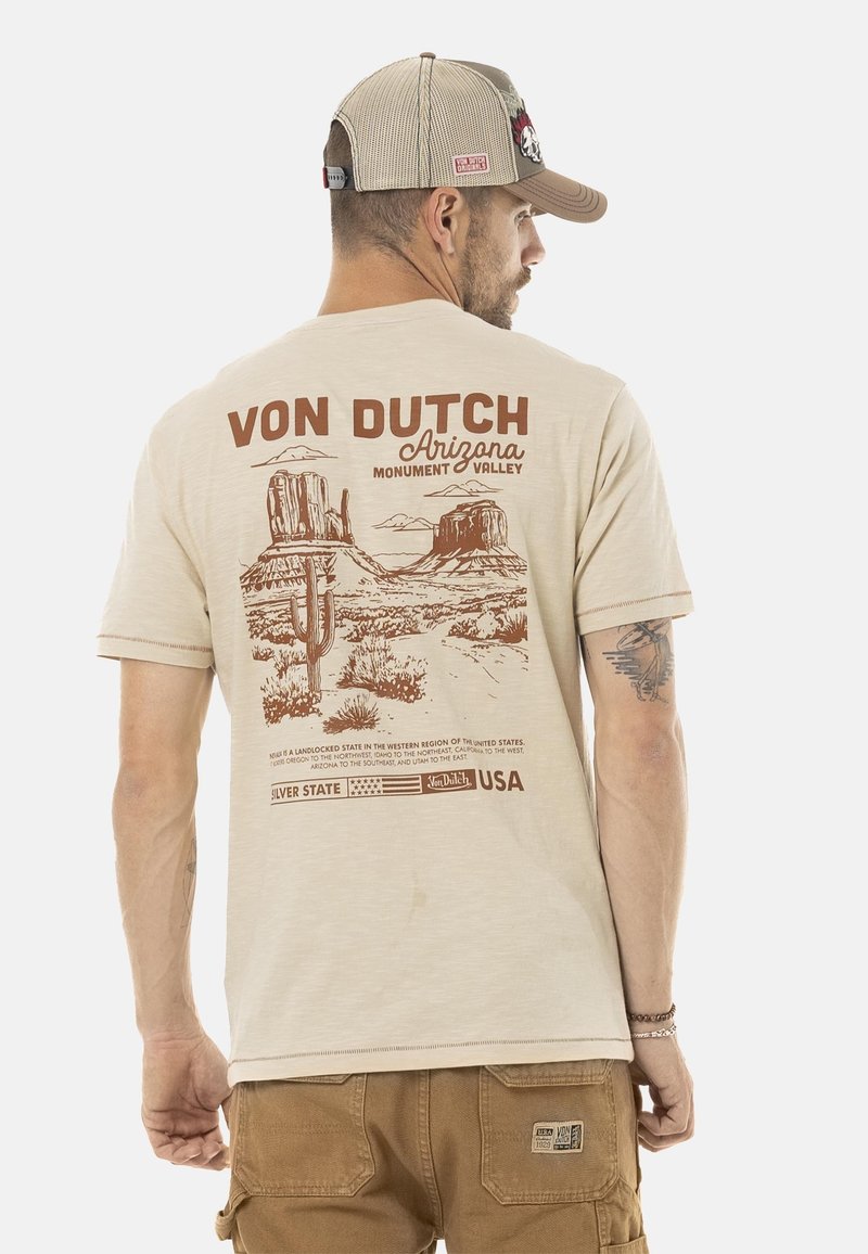 Camiseta de algodón beige con un gráfico marrón de monumentos del desierto y cactus. También incluye detalles de texto "VON DUTCH" y "Arizona".