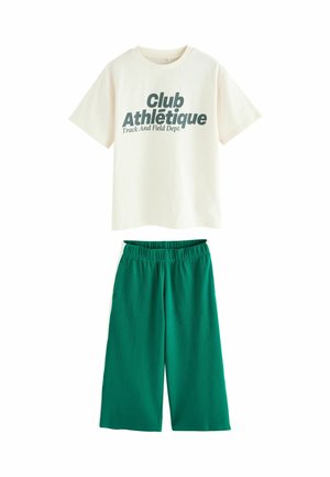Cremfarbener Baumwoll-T-Shirt mit dunkelgrünem Text "Club Athlétique Leichtathletik-Abteilung" kombiniert mit grünen weiten Shorts.