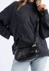 Schwarze Leder-Umhängetasche mit Nietenakzenten, geschwungener Form und verstellbarem Tragegurt. Die strukturierte, weiche Oberfläche ergänzt die lässige Kleidung.