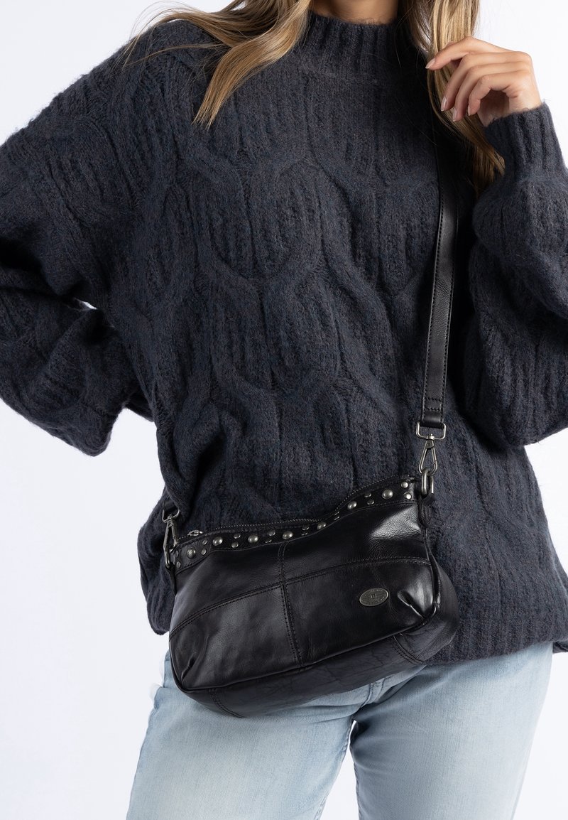 Schwarze Leder-Umhängetasche mit Nietenakzenten, geschwungener Form und verstellbarem Tragegurt. Die strukturierte, weiche Oberfläche ergänzt die lässige Kleidung.