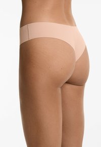 Lichtbeige stringondergoed met een naadloos ontwerp en een zachte, gladde textuur. De tailleband is dun en elastisch, die subtiel versmelt met de huidskleur.