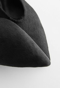 Mustadust mustad kingad, mis on valmistatud siledast, tekstuursest materjalist, millel on sile ja minimalistlik disain, kumerate joontega ja ilma nähtava kinnitusteta.