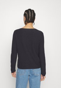 Pull noir à manches longues avec une texture côtelée et un col arrondi, associé à un jean denim bleu clair, vu de dos.