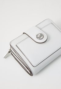 White leather wallet with a textured finish, featuring a metal snap closure and brown accent stitching along the edges. Zipper detail visible.