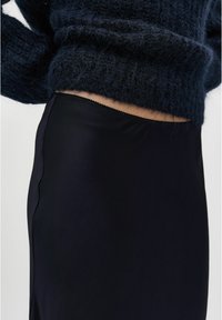 Gonna nera realizzata in tessuto liscio con un design elegante. Presenta un orlo scallop e viene indossata sotto un maglione navy a trama.