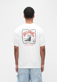 Λευκό βαμβακερό t-shirt με γραφικό τύπωμα στην πλάτη που απεικονίζει το "BILLABONG" με κόκκινα γράμματα, περιβαλλόμενο από διακοσμητικό πλαίσιο. Κοντά μανίκια, άνετη εφαρμογή.