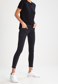 Camiseta de algodón negra combinada con jeans ajustados negros y zapatillas blancas. Los jeans tienen un diseño entallado y un ligero deshilachado en el dobladillo.