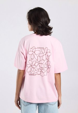 Persoon met donker haar die wegkijkt, draagt een roze T-shirt met een rood bloemmotief in lijntekening en de tekst "California Paradise" en "Endless Summer 1999."
