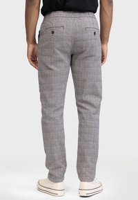 Pantaloni a quadrati grigi con vestibilità slim, cintura elastica e tasche posteriori, abbinati a scarpe da ginnastica di colore chiaro.