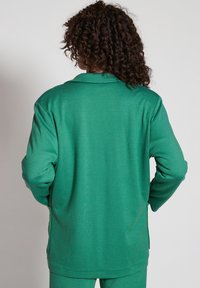 Grön stickad jacka med krage, som har lång ärmar och en avslappnad passform. Slät textur och sidofickor för komfort.