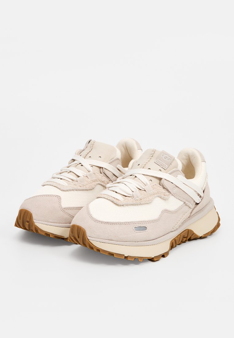 Baskets beiges en mélange de daim et de matières en maille, à bout arrondi, avec semelle en caoutchouc épaisse, lacets plats et détails d'accent sur le côté.