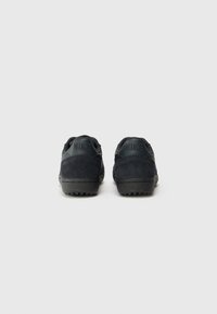 Zapatillas de ante y cuero negro con un acabado texturizado, que presentan un perfil bajo y un logo grabado en el talón. La suela de goma proporciona agarre.