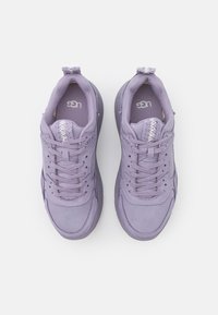 Violetti lenkkarit, joissa on sileä, teksturoitu pinta, nauhakiristys ja pehmustettu kaulus. Sisältää kontrastivärisen kudotun yksityiskohdan kantapään kunnassa.