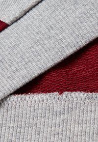 Tela texturizada gris y burdeos superpuesta, con un patrón de punto acanalado y costuras visibles a lo largo de los bordes.