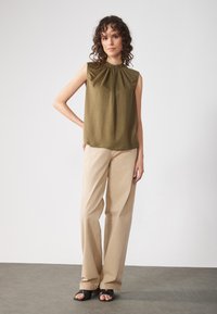 Olivgrön ärmlös topp med samlad halsringning, kombinerad med beige vida byxor och svarta sandaler. Slät textil, avslappnad passform.