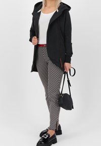 Sudadera negra con cremallera y capucha, sobre una camiseta blanca. Combinada con pantalones ajustados de estampado en blanco y negro y mocasines negros. Pequeño bolso negro.