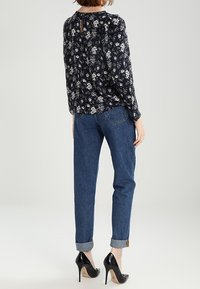 Granatowa kwiatowa bluzka z długimi rękawami i detalem na plecach z wycięciem, zestawiona z dżinsami z podwiniętymi mankietami i czarnymi szpilkami.