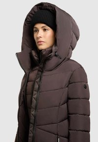 Polstret brun jakke med stor hætte og lynlås, der har en glat tekstur og sorte knapdetaljer på ærmet.