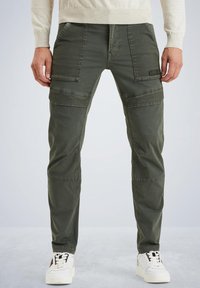 Olivgrüne Cargo-Hosen mit schmalem Schnitt, ausgestattet mit mehreren Taschen, genähten Akzenten und einer strapazierfähigen Stofftextur. Kombiniert mit weißen Sneakern.