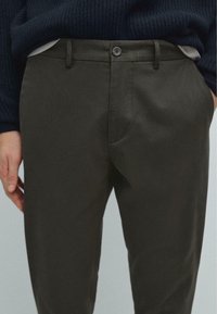 Mørkegrønne chinos lavet af et glat stof, med en knaplukning, sidelommer og en lige benklipp.