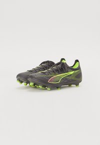 Botas de fútbol negras y verde neón con una parte superior texturizada, cierre de cordones y tacos moldeados para tracción en superficies de hierba.