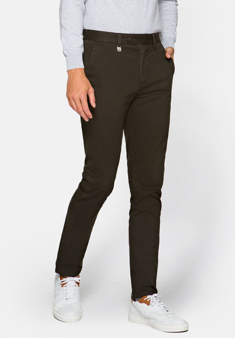 Ciemnozielone slim fit chinosy o gładkiej strukturze, z zamkiem błyskawicznym i kieszeniami z przodu. Dobrane z białymi trampkami i jasnoszarym topem z długim rękawem.