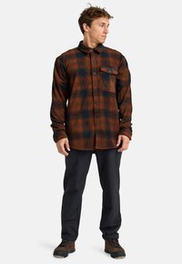 Karierte Flanellhemden in verschiedenen Orangetönen und dunklem Grün, mit durchgehender Knopfleiste, einer Brusttasche und langen Ärmeln. Getragen mit schwarzen Hosen und Stiefeln.