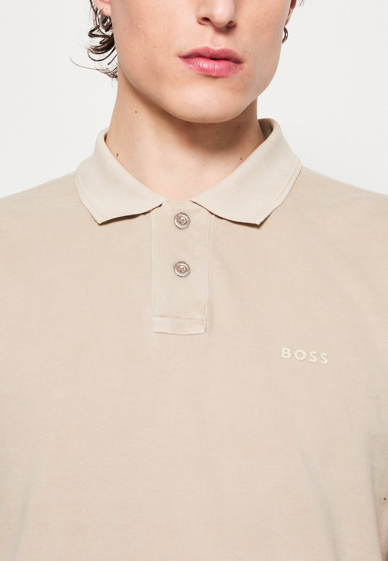 Polo color beis de algodón con cuello clásico, dos botones y sutil logo "BOSS" bordado en el pecho.