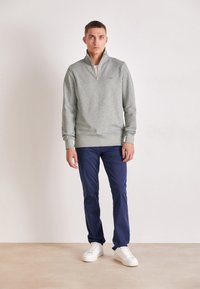 Felpa grigia con zip e polsini a coste, abbinata a pantaloni navy e sneakers bianche. Design semplice e casual con una texture liscia.