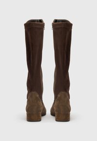 Bottes en suède marron montant jusqu'au genou avec une texture douce, dotées d'une fermeture éclair noire sur le côté et d'un talon empilé, présentant un design lisse.