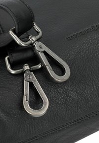 Due chiare fibbie metalliche d'argento attaccate a una tracolla in pelle nera testurizzata e a una borsa con cuciture visibili.
