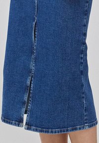 Jeanskjørt i mørkeblått med rett snitt, med en frontsplitt, frynset søm og kontrasterende sytråd.