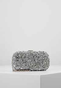 Kompaktowa srebrna kopertówka ozdobiona różnorodnymi cyrkoniami, perłami i cekinami, z łańcuszkowym paskiem i metalowym zapięciem.