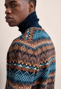 Strickpullover mit hohem Marinekragen, verziert mit geometrischen Mustern in Brauntönen, Türkis und Cremetönen.