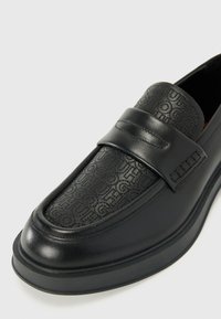 Juodi odiniai loafersai su iškiliais raštais viršuje, elegantiškas dizainas, plati juosta per pėdos vidurį ir tekstūruotas padas.
